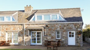 A stone building with a large patio area, a seating arrangement, and a door labeled "GLAS HOUSE." - Tyn Towyn - Ty Glas Golau (Holyhead)