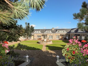 A stone building with a well-maintained lawn, a fountain, and a variety of flowers. - Tyn Towyn - Ty Glas Golau (Holyhead)