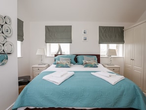 A neatly arranged bedroom with a bed, two bedside tables, a window with a view, and a wardrobe. - Tyn Towyn - The Stables (Holyhead)
