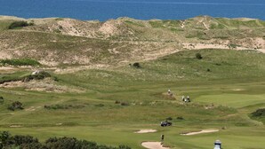 Ein Golfplatz mit Bunkern, einer Fahne und einem Leuchtturm in der Ferne.