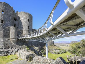 Un château en pierre relié à une zone verdoyante par un pont piétonnier moderne.