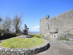 Un mur de pierre surmonté d’une statue d’un homme à cheval, une zone herbeuse et un ciel dégagé.