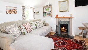 Ein gemütliches Wohnzimmer mit Kamin, einer Couch mit gemusterten Kissen, einem Bücherregal und einem an der Wand befestigten Flachbildfernseher.