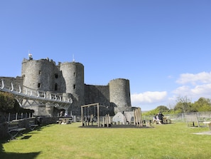 Un château historique doté de deux tours imposantes, d’une allée pavée et d’une cour verdoyante agrémentée de bancs.
