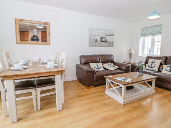 A furnished living room with a dining area, a brown leather sofa, a coffee table, and a painting on the wall. - Bayside Cottage (Filey)