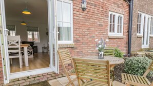 A patio with wooden chairs and a table, a brick building with windows, and a door leading to an interior space. - Bayside Cottage (Filey)