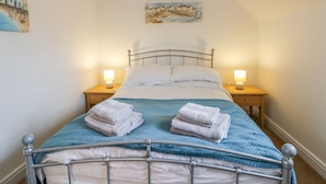 A neatly made bed with a blue blanket and two folded towels on each side, a metal-framed bed, and two bedside lamps on wooden nightstands. - Bayside Cottage (Filey)