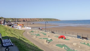 A coastal area with a sandy beach, a small park with green play areas, and a few benches. - Bayside Cottage (Filey)