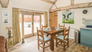 Un coin repas accueillant avec une table et des chaises en bois, une horloge au mur et une vue sur le jardin par la porte vitrée.