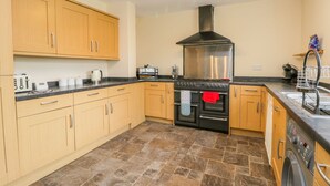 A modern kitchen with wooden cabinets, a stainless steel range hood, a built-in oven, a dishwasher, and a washing machine. - 5 Cliff Lane (Bridlington)