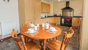 A dining area with a wooden table and chairs, a kitchen with wooden cabinets and a black stove, and a wall clock. - 5 Cliff Lane (Bridlington)