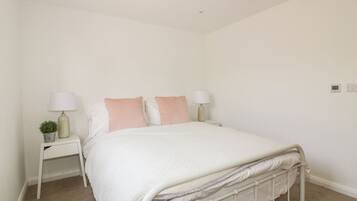 A bedroom with a single bed, two bedside tables, each with a lamp and a small plant.
