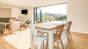 A spacious living room with a large dining table, comfortable seating, a flat-screen TV, and a view of the outdoors. - The Beach Halt (Perranporth)