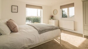 A bedroom with a bed, a dresser, a radiator, and two windows. - The Beach Halt (Perranporth)