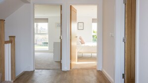 A hallway leading to a bedroom with a bed, a framed picture on the wall, and a wooden door. - The Beach Halt (Perranporth)