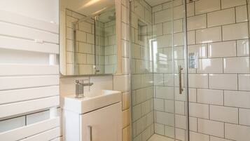 Un baño moderno con ducha envuelta en vidrio, un lavabo blanco y un espejo grande.