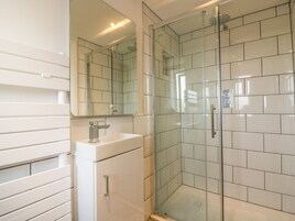Un baño moderno con ducha envuelta en vidrio, un lavabo blanco y un espejo grande.