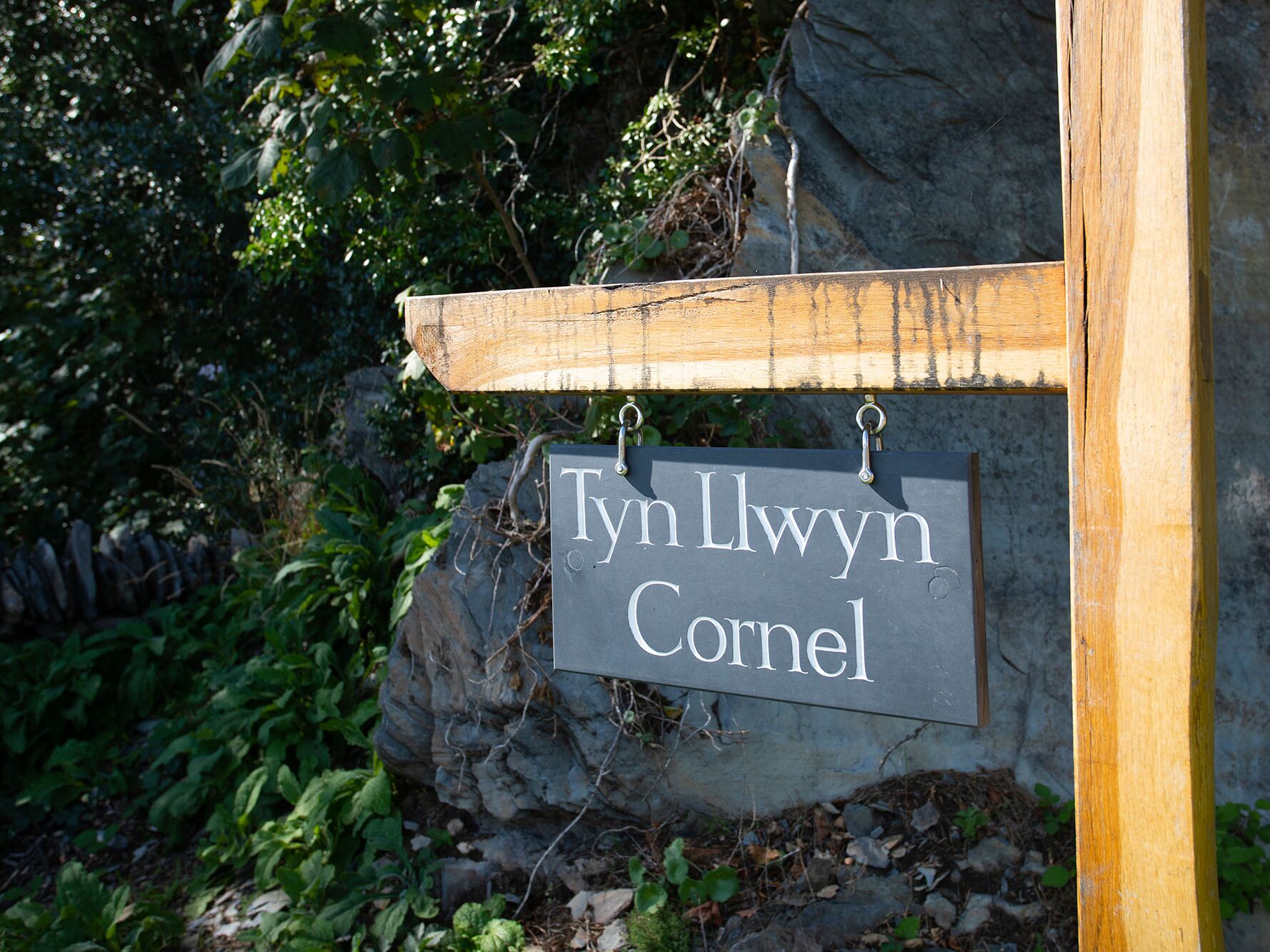 A sign with the name "Tyn Llwyn Cornel" mounted on a wooden post.