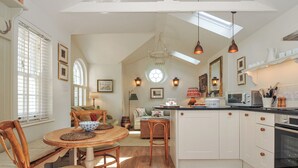 A kitchen with white cabinets, a dining area with a wooden table and chairs, and a central island with a sink. - The Coach House at Pendower House (Fowey)