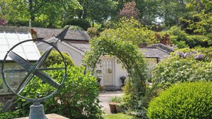 A garden with a sundial, a house with a white facade, and a green lawn. - The Coach House at Pendower House (Fowey)