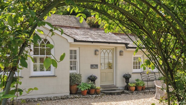 A quaint cottage with a white facade, a small porch with potted plants, and a gravel driveway. - The Coach House at Pendower House (Fowey)