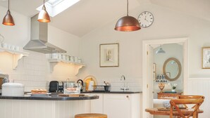 A kitchen with a central island, white cabinetry, and copper pendant lights. - The Coach House at Pendower House (Fowey)