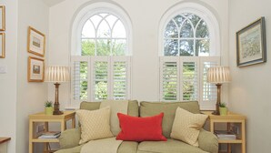 A cozy room with a green sofa, two windows with shutters, and a framed picture on the wall. - The Coach House at Pendower House (Fowey)