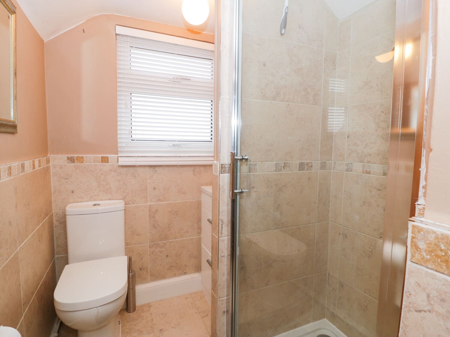 A bathroom with a toilet, a shower with glass doors, and a window with blinds.
