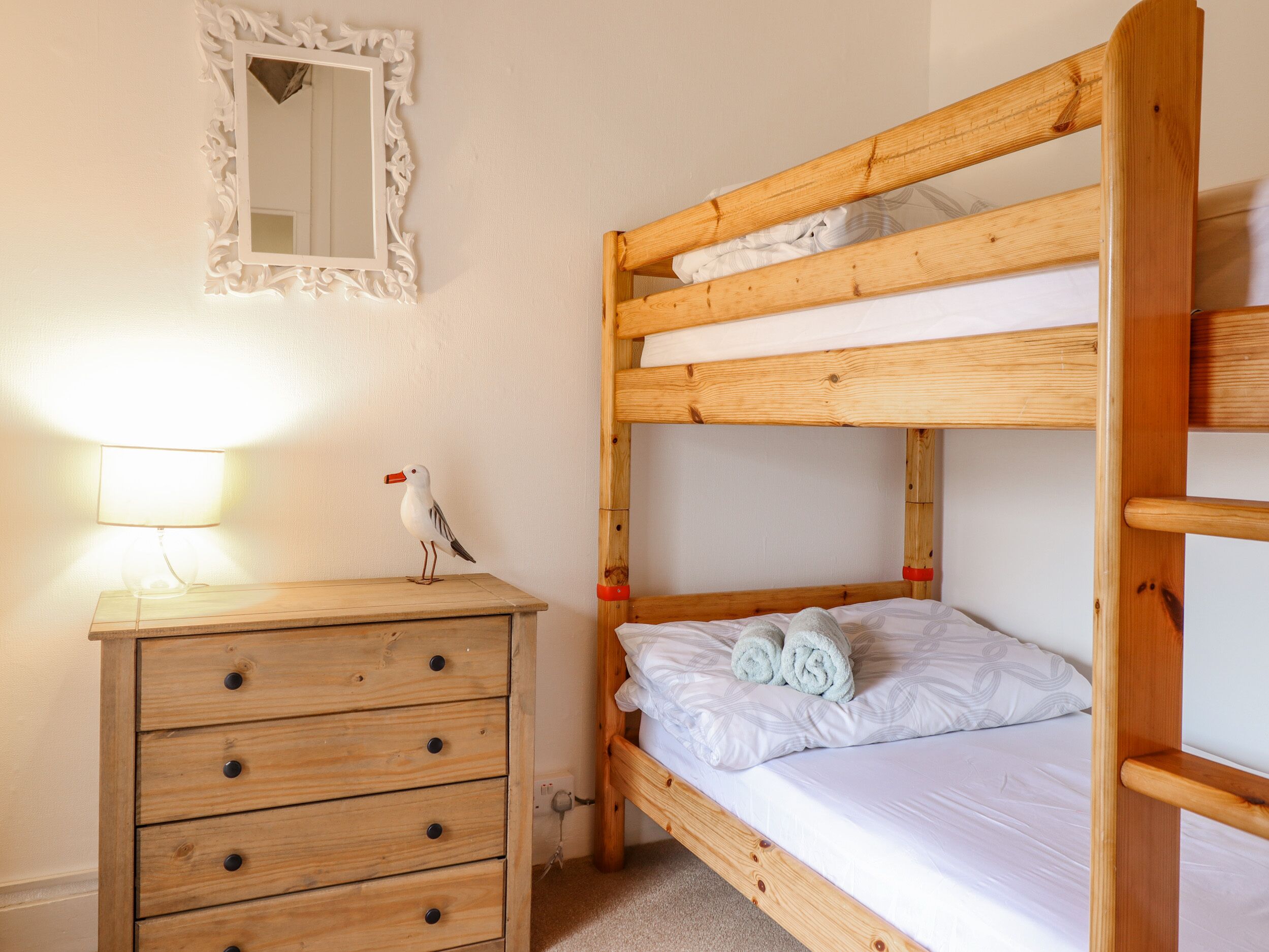 A bunk bed with a wooden headboard, a dresser with drawers, a mirror, and a lamp.