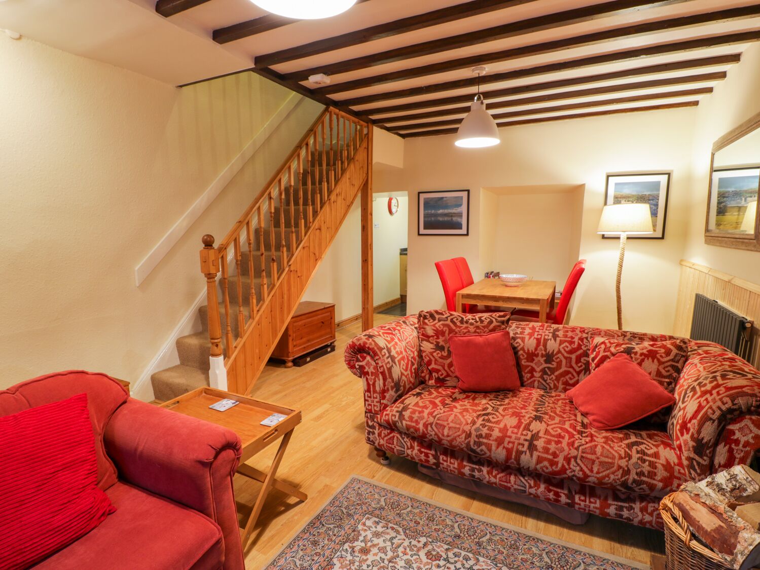 Ein Wohnzimmer mit einer Holztreppe, einem gemusterten Sofa, einem Esstisch mit Stühlen und einer Lampe.