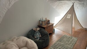Una habitación acogedora con suelo de madera, un sillón informal grande y mullido, un pequeño aparador de madera y una tienda tipi.