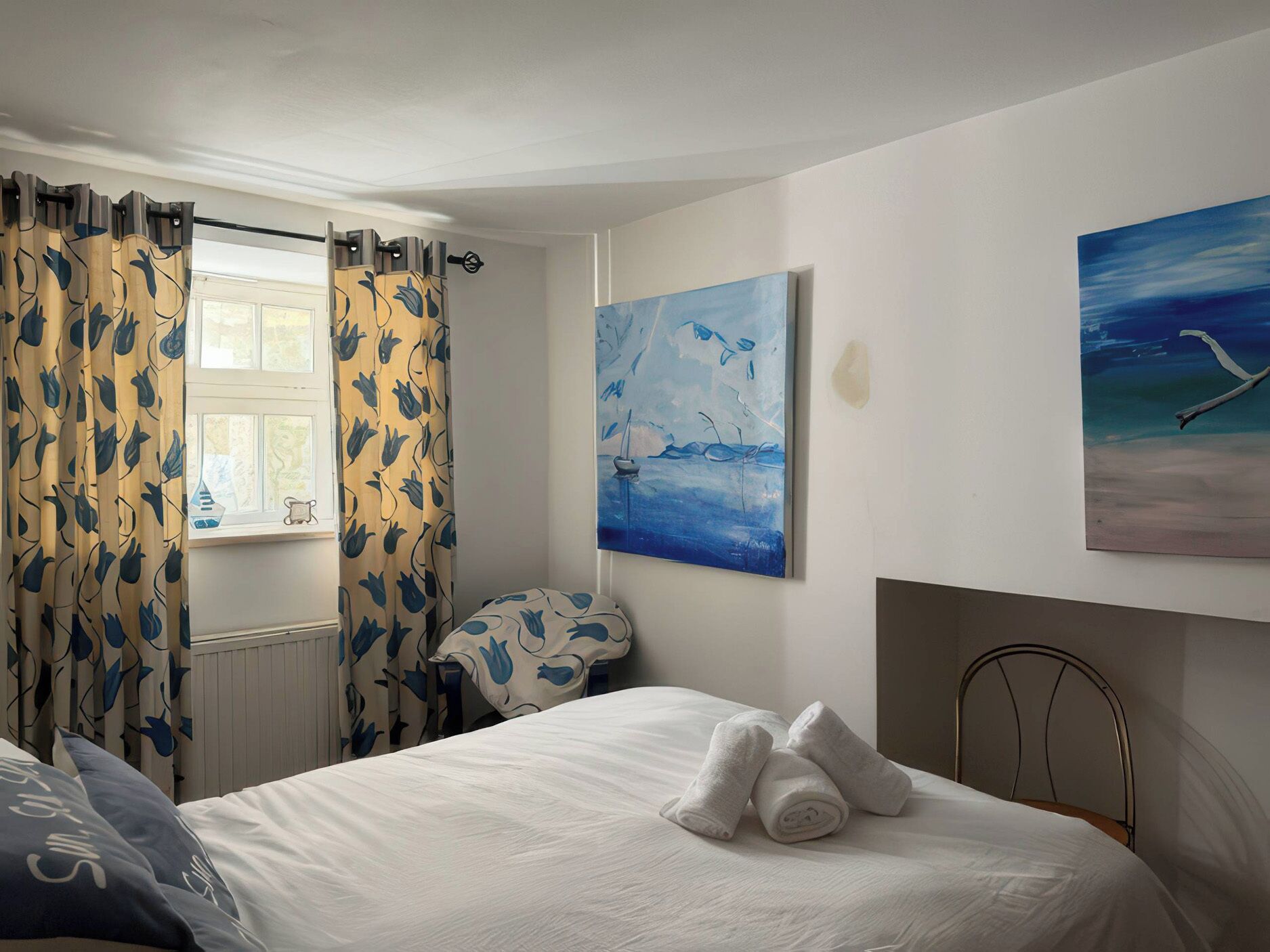 A bedroom with a bed, a window with curtains, a painting, and a fireplace.