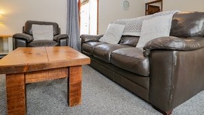 A living room with a brown leather sofa, a wooden coffee table, and a grey carpet. - Raygill Cottage (Whitby)