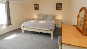 A bedroom with a bed, bedside tables, a dresser, a mirror, and two paintings on the wall. - Raygill Cottage (Whitby)