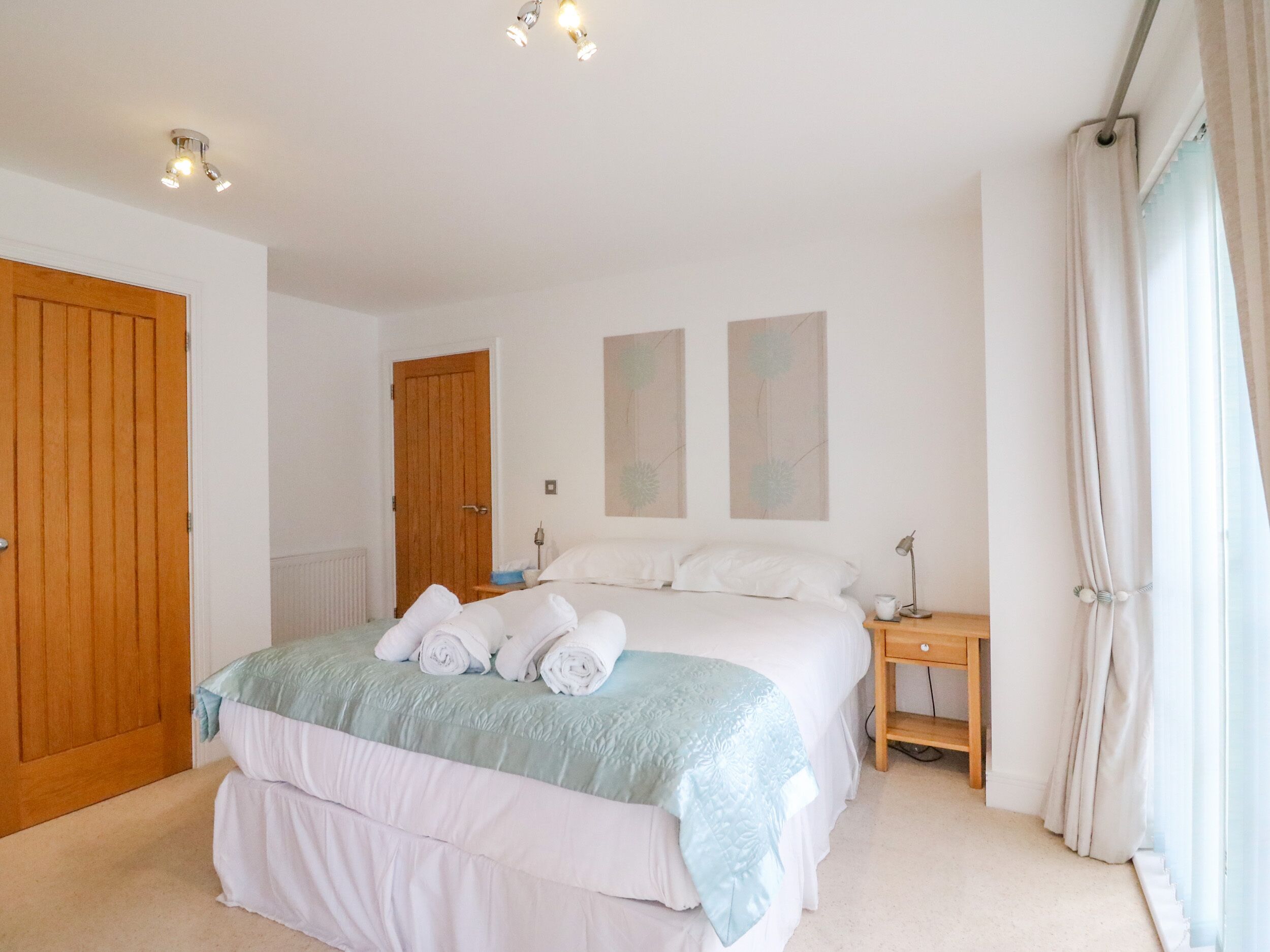 Een slaapkamer met een bed, een houten deur, een nachtkastje en een raam met gordijnen.