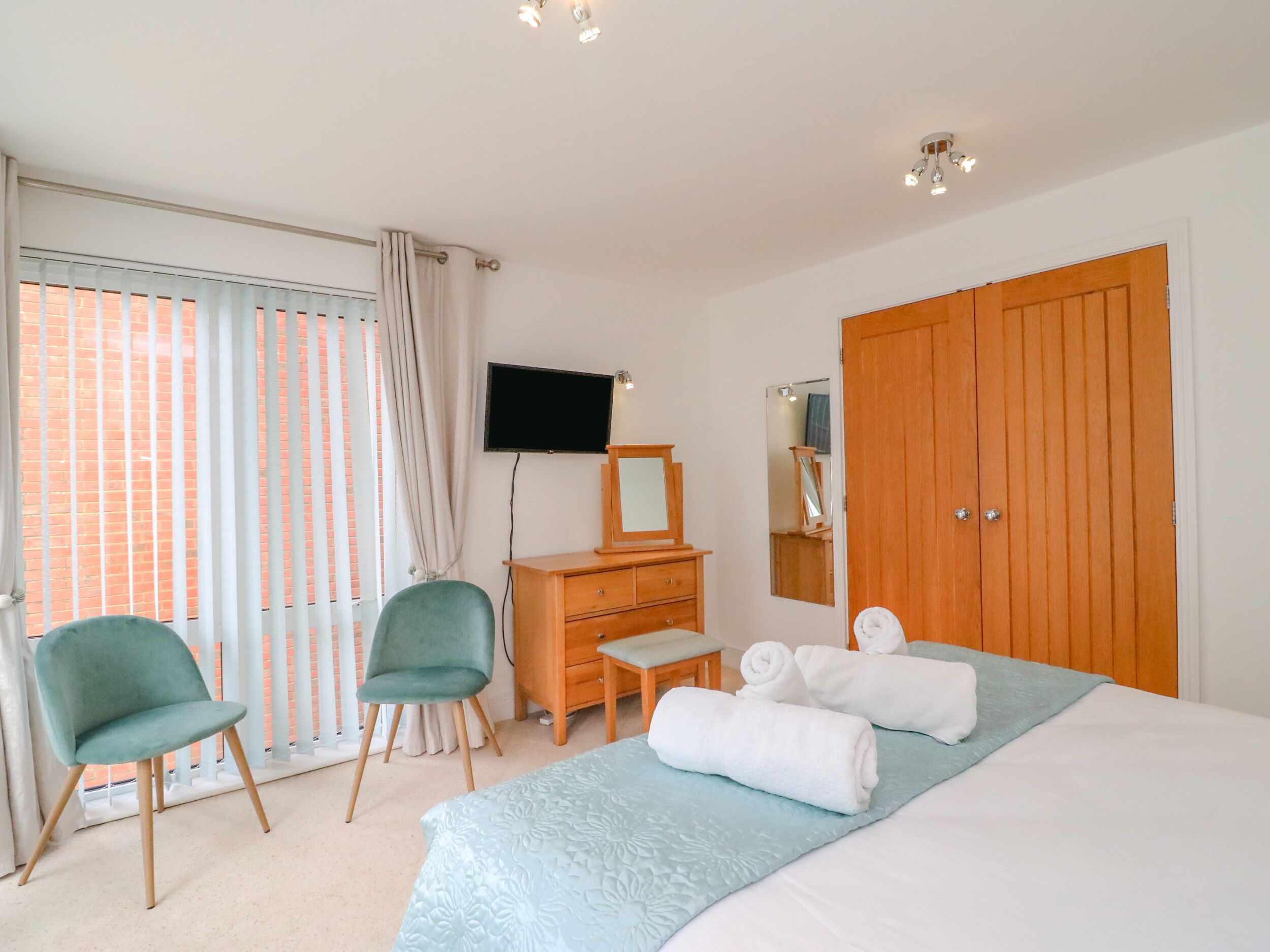 A bedroom with a bed, two chairs, a dresser, a television, and a wardrobe.