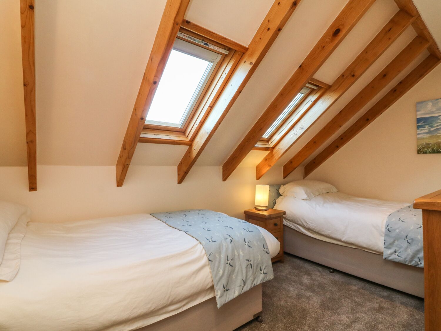 A bedroom with two beds, a skylight, and a painting on the wall.