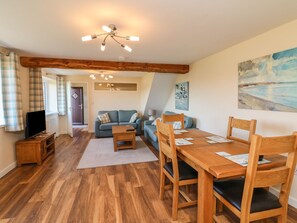 A cozy living room with a wooden ceiling, a dining table with chairs, a sofa, and a television on a wooden stand. - Rose Cottage (Barnstaple)