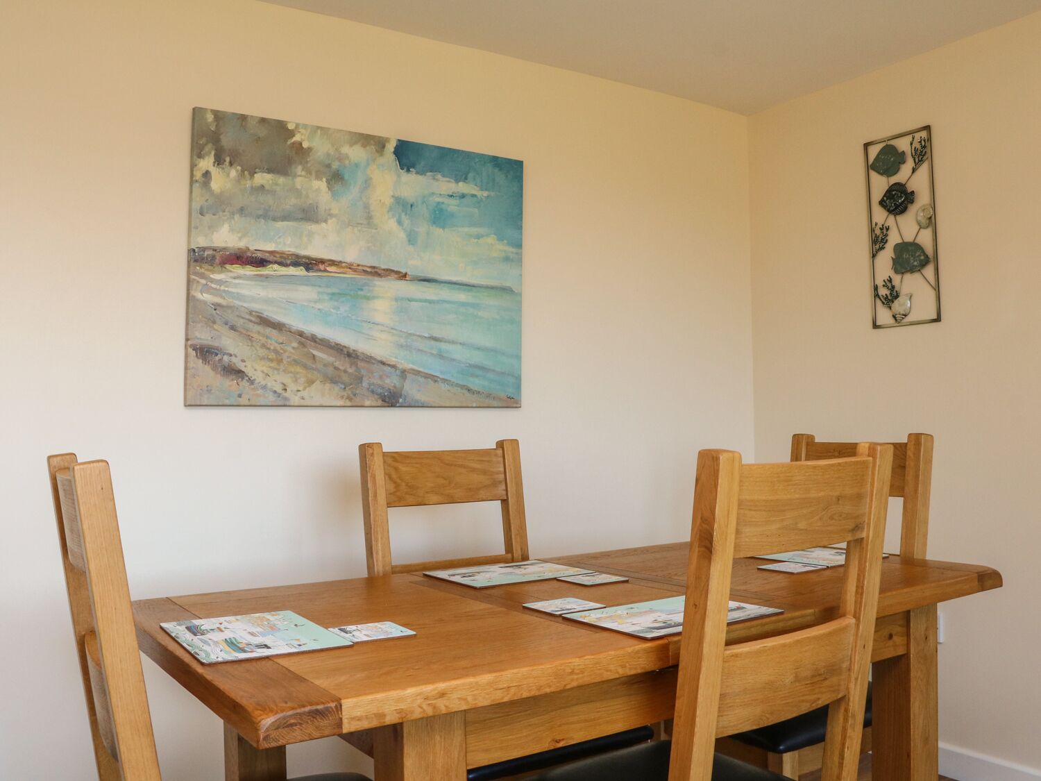 A dining area with a wooden table and chairs, a painting of a beach scene, and a decorative metal piece on the wall.