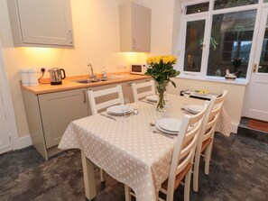 Een kleine keuken met een eettafel voor vier personen, een magnetron en een raam met uitzicht op groen.