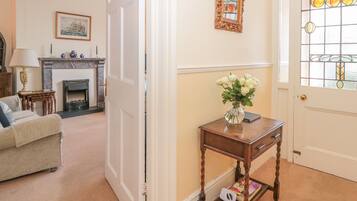 A living room with a sofa, a fireplace, a table with a vase of flowers, and a door with a stained glass window.