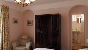 Camera da letto con un letto grande, un armadio, una sedia e un bagno visibile attraverso una porta aperta.