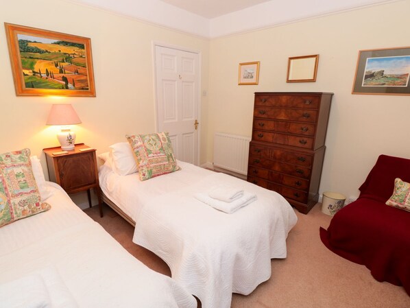A room with two single beds, a dresser, a lamp, and a door.