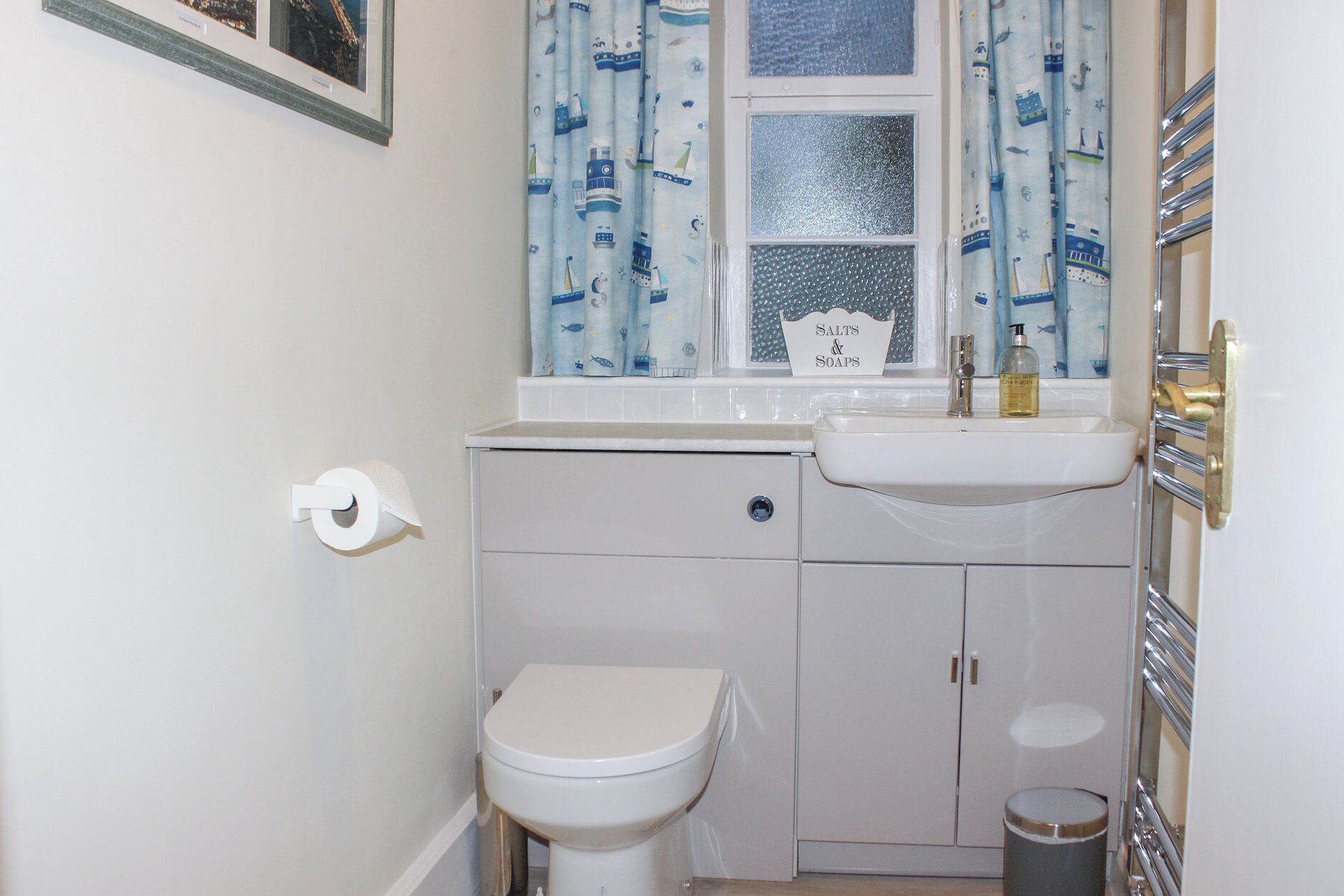 A small, compact bathroom with a toilet, a sink, and a window with curtains.