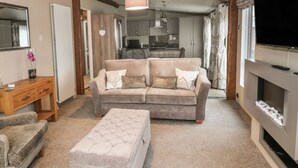 A living room with a sofa, ottoman, wooden side table, and a TV. - Avonal Lodge (Perth)