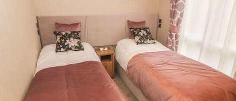 Una habitación doble con dos camas, cada una con cubrecama marrón y almohadas estampadas. Encima de las camas hay dos cuadros enmarcados.