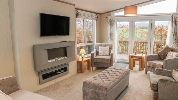 A modern living room with a flat-screen TV, a fireplace, comfortable seating, and a balcony with a view. - Avonal Lodge (Perth)