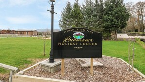 A sign for Lochmanor Holiday Lodges in a landscaped area with a lamp post, trees, and a building in the background. - Avonal Lodge (Perth)