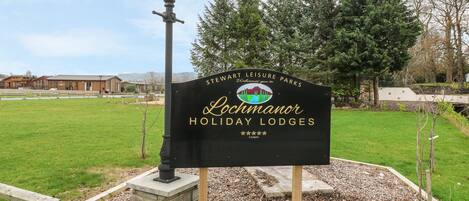 A sign for Lochmanor Holiday Lodges in a landscaped area with a lamp post, trees, and a building in the background.