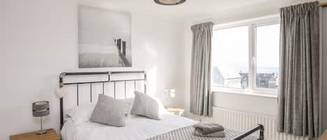 A bedroom with a bed, bedside table, lamp, and a window with curtains.